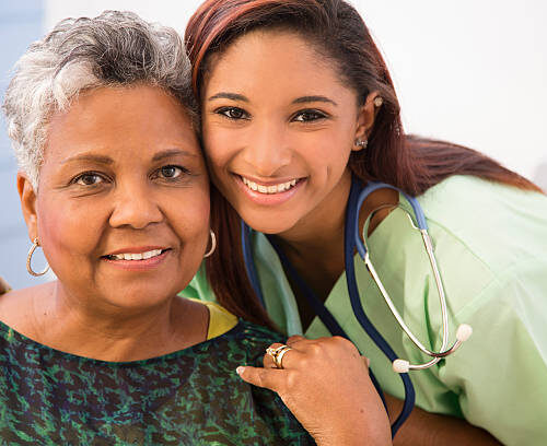 Caring, mixed-race nurse or care giver gives a senior adult, African descent patient a reassuring hug in hospital or clinic setting.  Headshot.
